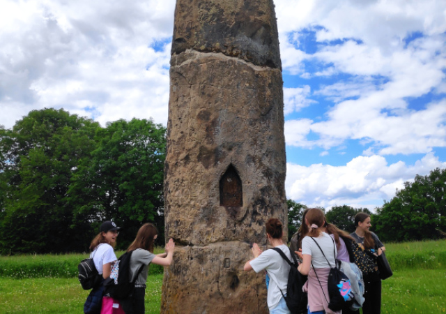 Uczniowie stoją dookoła neolitycznego menhiru – skalnego monumentu o nazwie Gollenstein